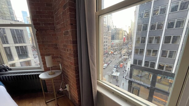 A room with a large window overlooking a busy street, a small table with a lamp, and a radiator on the floor. - Nest Aparthotel kitchenette  (New York)