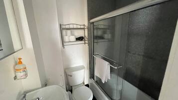 Un baño con inodoro, bañera y ducha con mampara de vidrio.