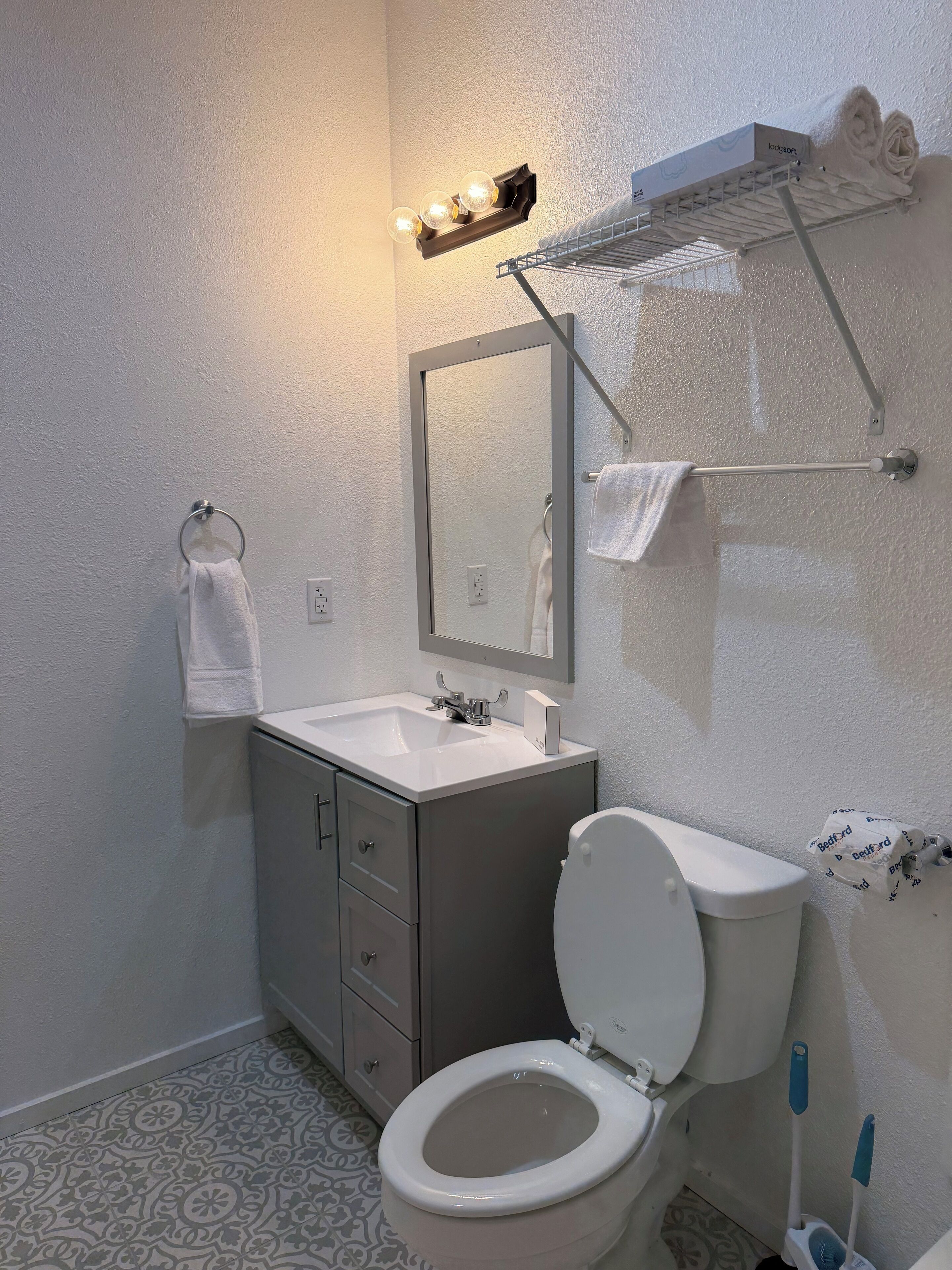 A bathroom with a toilet, sink, mirror, towel rack, and a shower area with a towel rack.