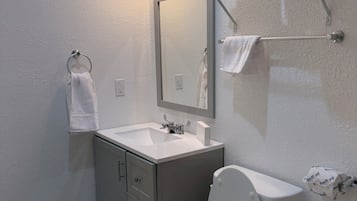 A bathroom with a toilet, sink, mirror, towel rack, and a shower area with a towel rack.