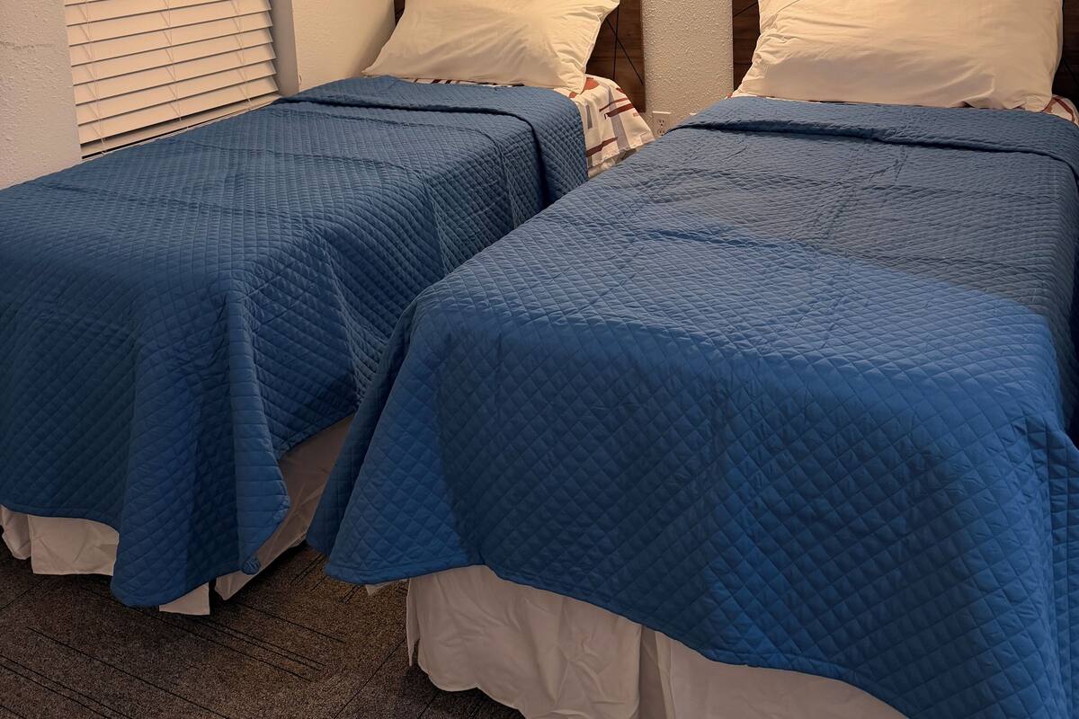 Une chambre d’hôtel avec deux lits, chacun recouvert d’une courtepointe matelassée bleue et agrémenté d’oreillers blancs. Deux appliques murales sont fixées au mur au-dessus des lits.