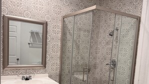 A bathroom with a vanity, a shower with a glass door, and patterned tiles on the walls and floor.