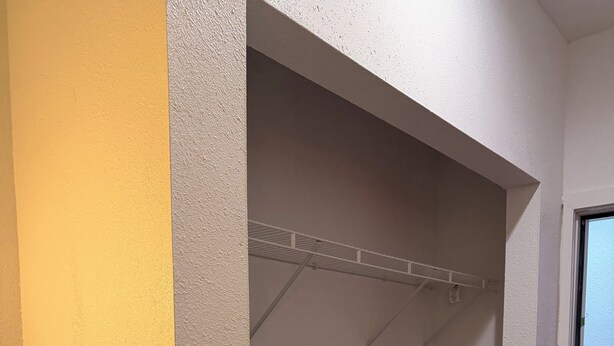 Ein Zimmer mit grauem Teppich, einer weißen Tür und einer weißen Wand mit strukturiertem, grauem Bereich.