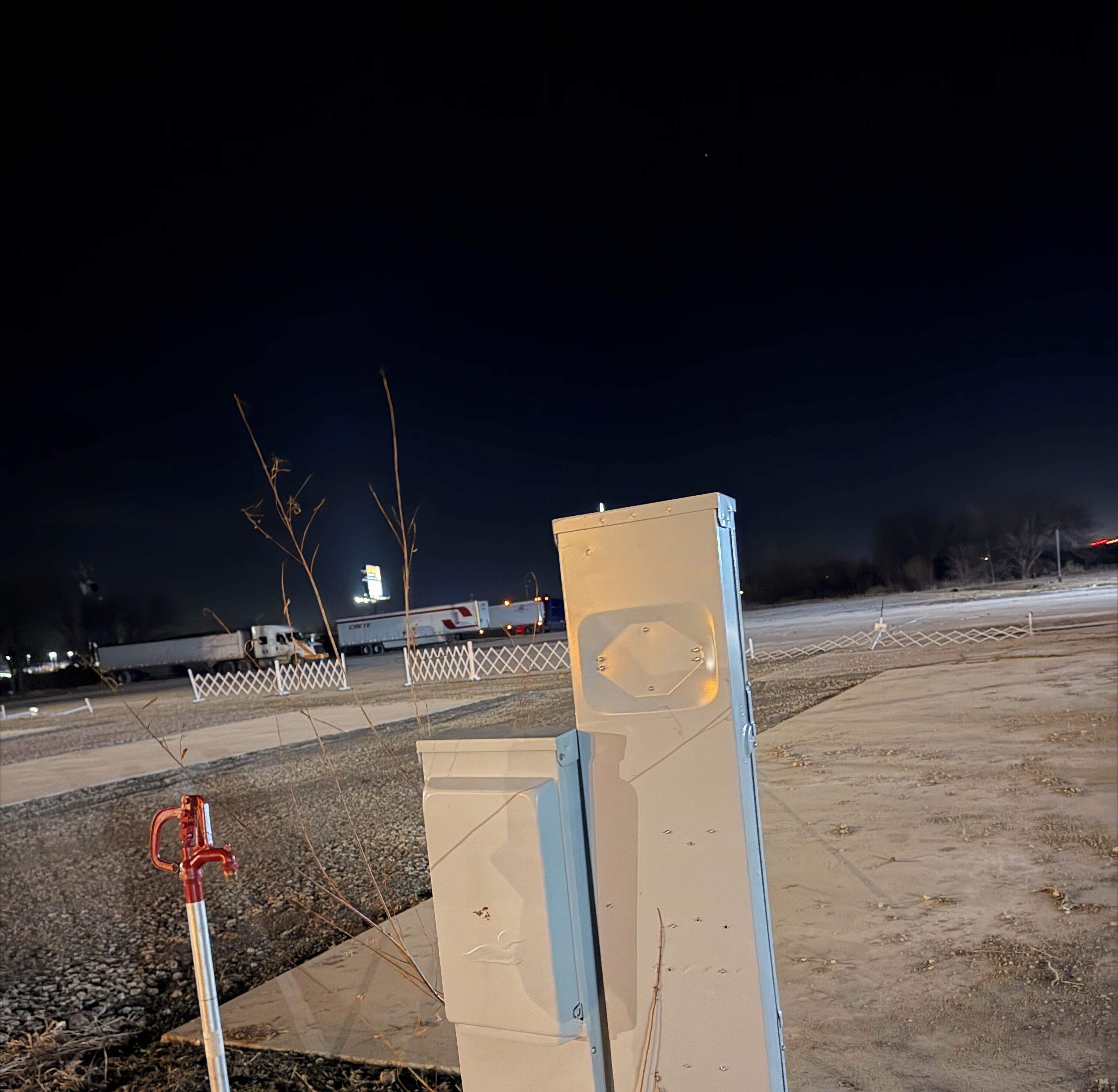 A parking lot at night with a few trucks and a white fence.