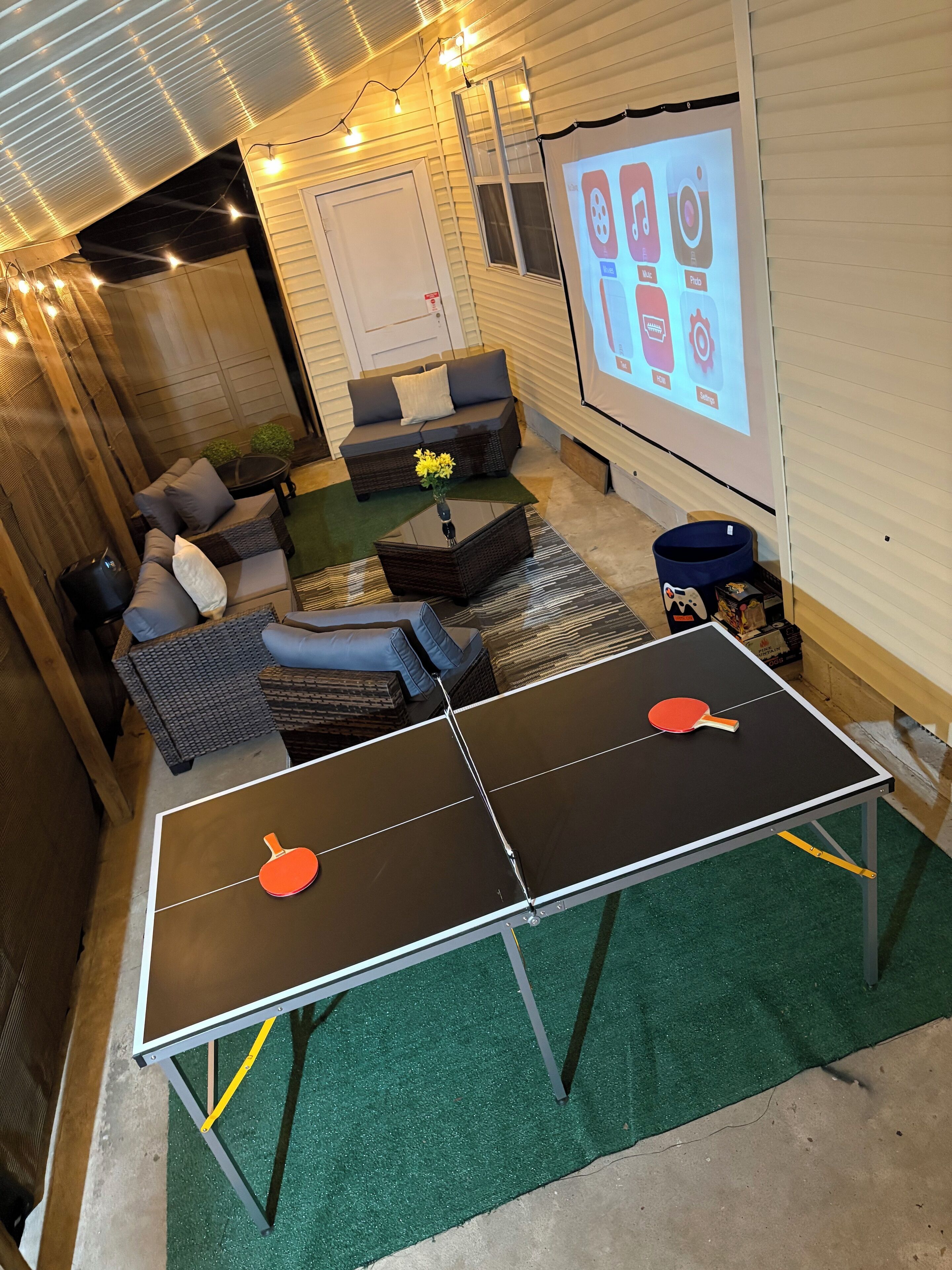 Ett inomhusområde för rekreation med bordtennisbord, sittplatser och en projektionsskärm som visar ikoner från olika appar.