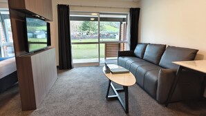 Un salon moderne comprenant un canapé, une petite table, un téléviseur à écran plat fixé sur un panneau en bois, et une porte-fenêtre coulissante donnant sur un espace extérieur.