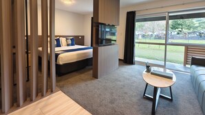 Une chambre d’hôtel moderne équipée d’un lit, d’une télévision, d’une petite table et d’une grande fenêtre donnant sur l’extérieur.