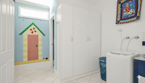 Een badkamer met een witte wastafel, een wit toilet en een witte inloopkast. Boven het toilet hangt een kleurrijk schilderij.