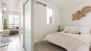 Un dormitorio moderno con una cama grande, un escritorio y una puerta de vidrio que da a una sala de estar.