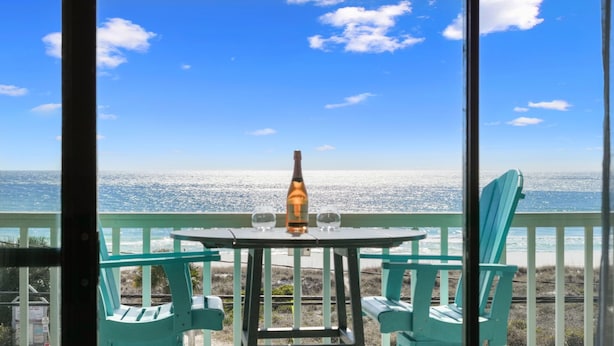 Un balcón con mesa y sillas con vista a la playa.
