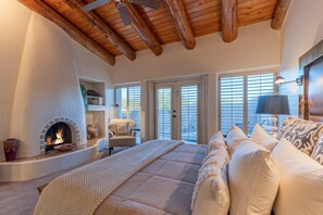 A cozy bedroom with a fireplace, a bed with patterned bedding, a chair, and a view through the door. - Near Boulder Resort & Spa, Greens Space & Views, Covered Patio w/Grill (Scottsdale)