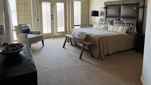 Un dormitorio con una cama grande, un banco, una silla, una mesita de noche y un frutero con fruta.