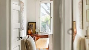 Un pasillo estrecho que conduce a un dormitorio con una cama, una mesita de noche y una ventana.