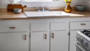 Una cocina con ventana, armarios blancos, estufa y una lámpara colgante.