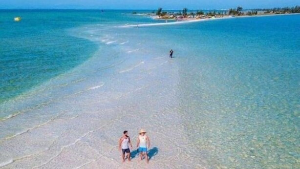 A beach with clear shallow waters and a distant shoreline.