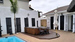 Een zwembad met een houten terras, een jacuzzi en een patio tafel met stoelen.