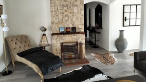 Een moderne woonkamer met een stenen openhaard, een gestoffeerde fauteuil, een eethoek met barstoelen en een grote vaas.