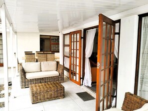 Ein Zimmer mit einem Rattan-Sofa, passendem Hocker und einer Schiebeglastür, die auf einen Balkon führt.