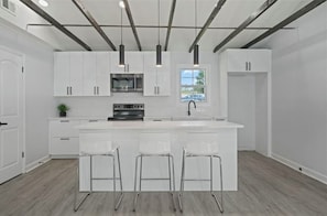 Une cuisine moderne avec des meubles blancs, un îlot central doté de tabourets, un four encastré et des luminaires suspendus.