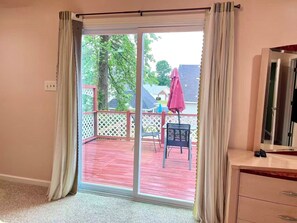 Une pièce dotée d’une porte-fenêtre coulissante donnant sur une terrasse extérieure avec un plancher en bois rouge, une clôture en treillis blanche et un parasol rose.