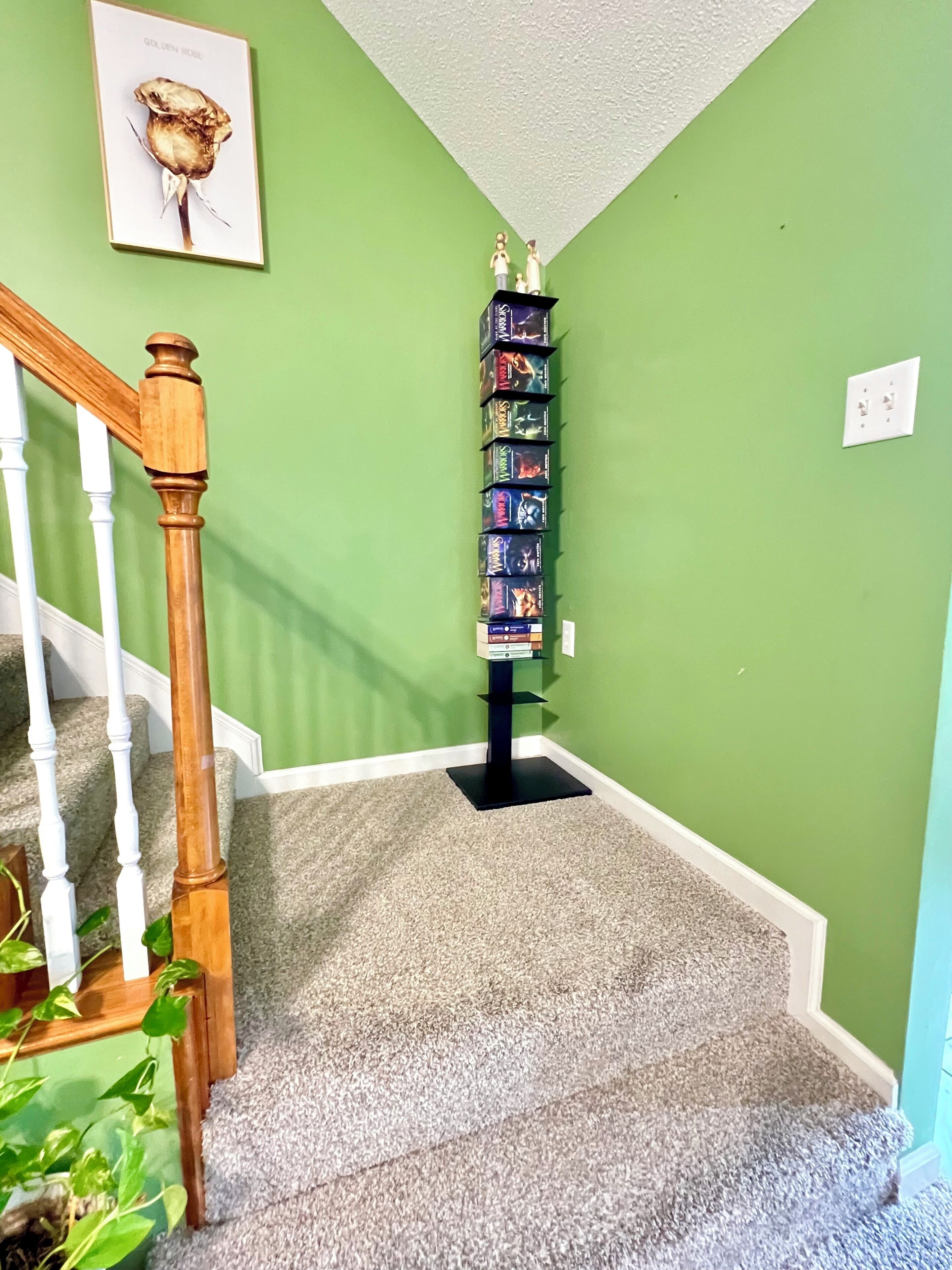 A carpeted staircase with a wooden handrail, green walls, a black bookshelf, and a framed picture on the wall.
