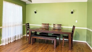 A dining area with a wooden table and chairs, a bench, and a window with sheer curtains. - Charming Home with Prime Augusta Location - Walk to Augusta National! (Augusta)