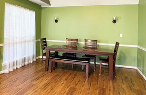 Un coin repas avec une table et des chaises en bois, un banc et une fenêtre ornée de rideaux légers.