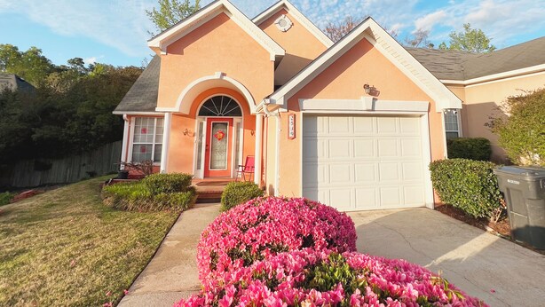 A two-story house with a red front door, a garage, and a well-maintained front yard with pink flowers. - Charming Home with Prime Augusta Location - Walk to Augusta National! (Augusta)