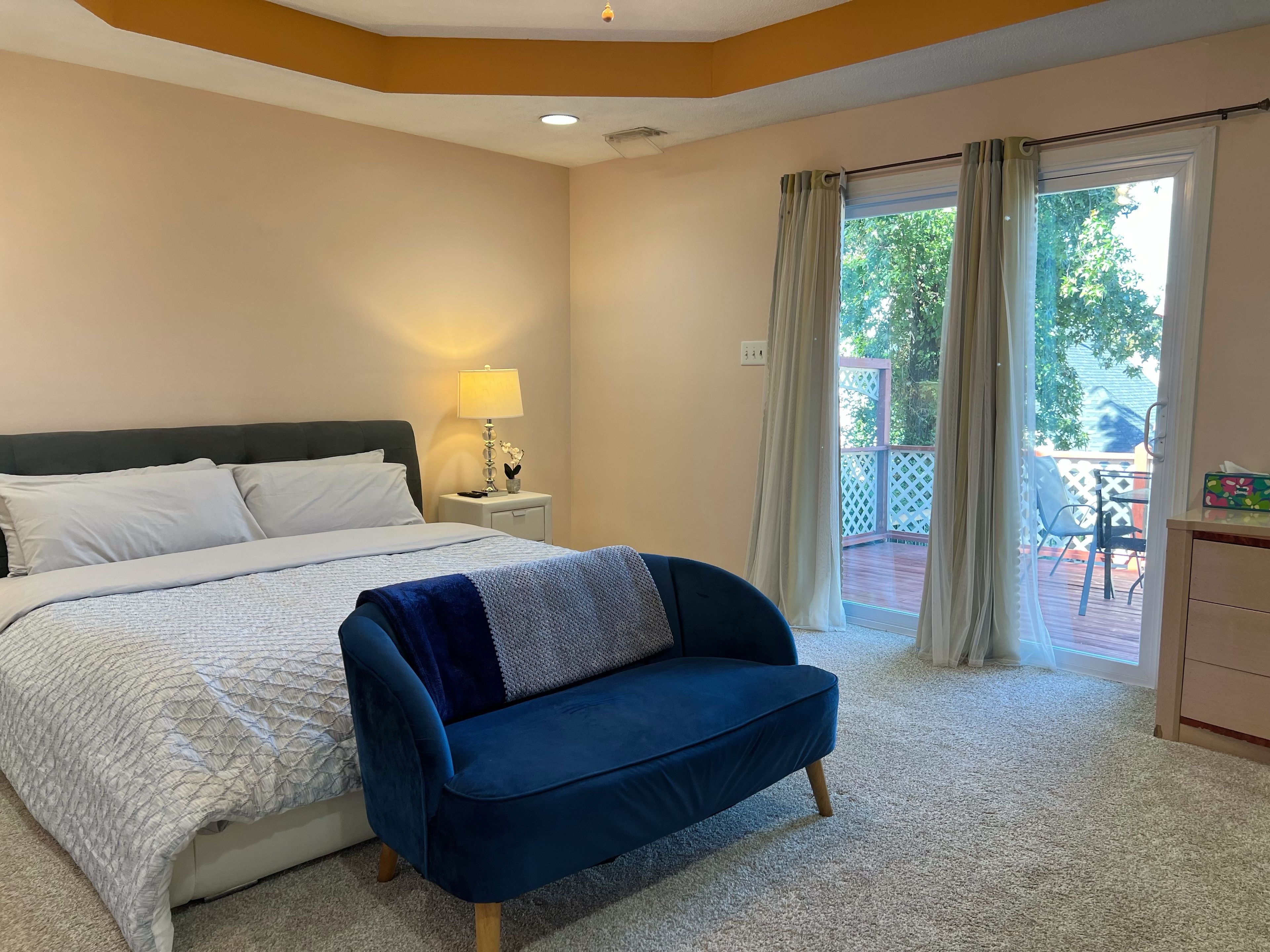 A bedroom with a bed, a nightstand, a lamp, a blue chair, and a balcony with a table and chairs.