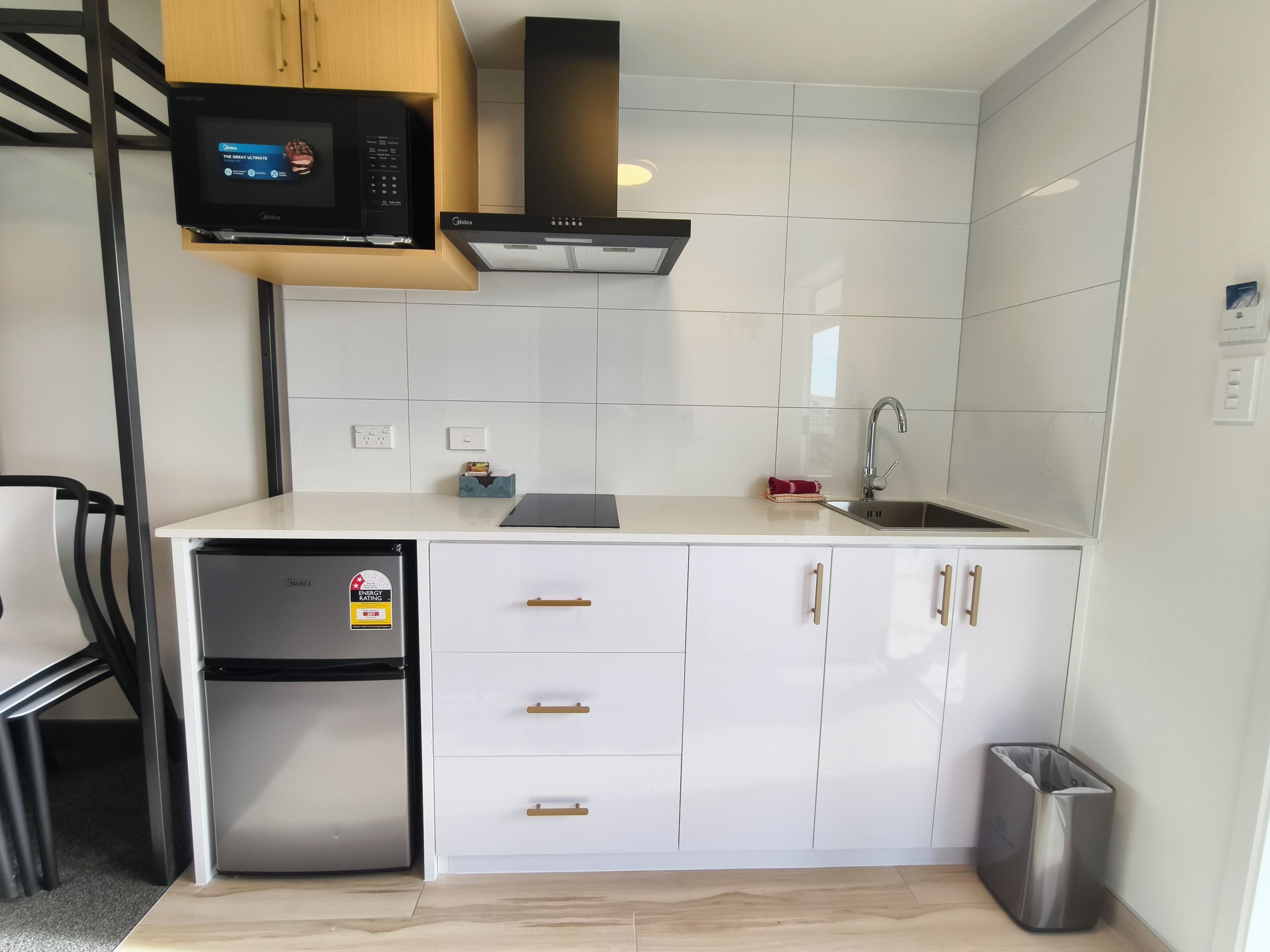 A compact kitchen with white cabinetry, a built-in microwave, a stainless steel refrigerator, and a sink.
