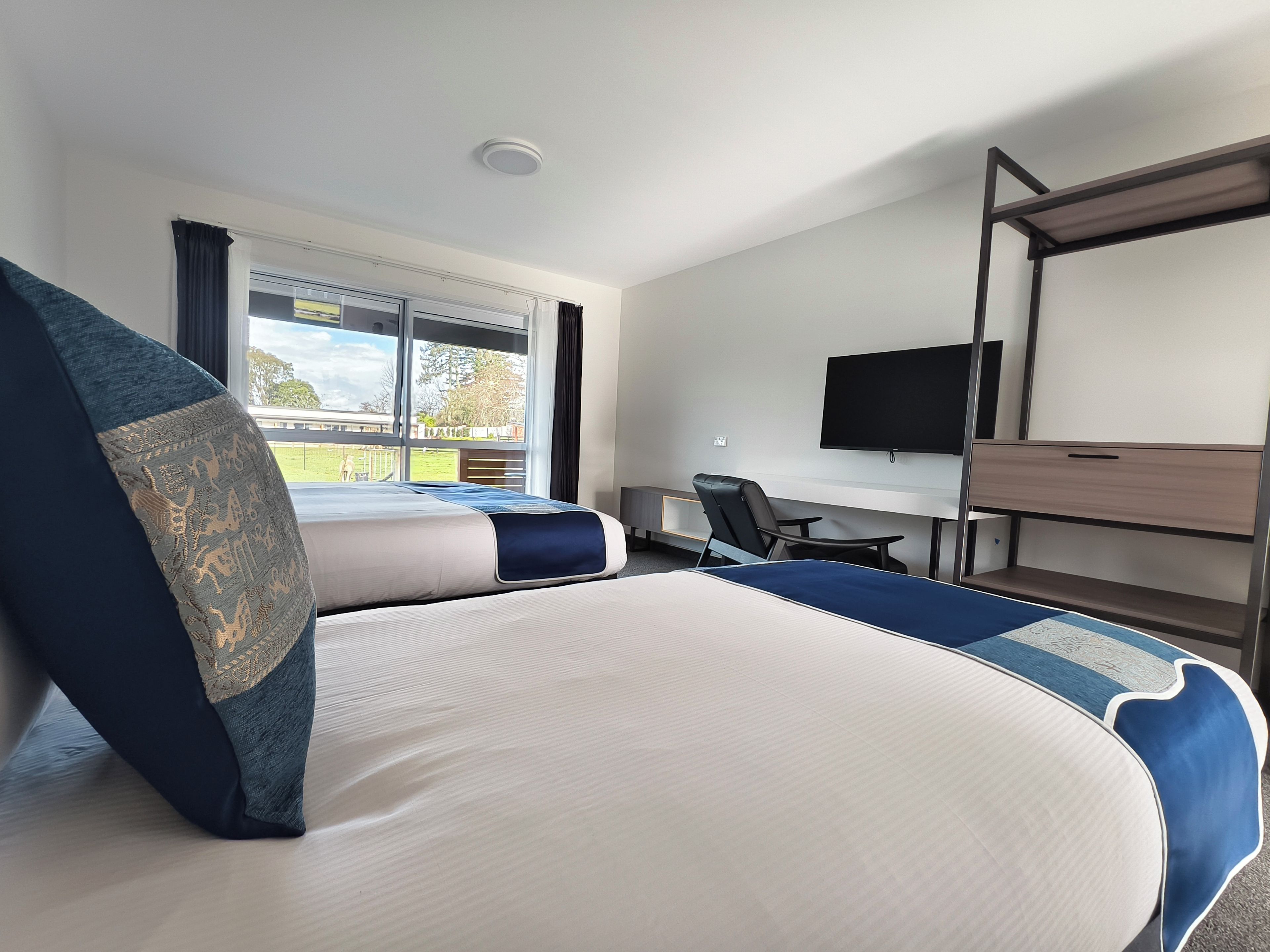 A hotel room with a bed, a desk, a chair, a television, and a window with a view of the outdoors.