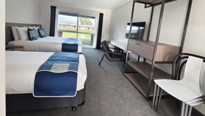 Une chambre d’hôtel avec deux lits, un bureau, une chaise, une télévision et un balcon avec vue.