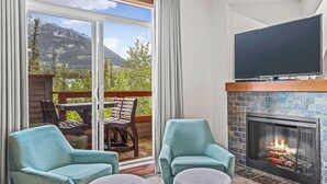 Een woonkamer met een open haard, een televisie en uitzicht op bergen door een schuifdeur.