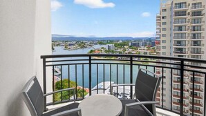 En balkon med bord og stole, udsigt over en flod og bybillede.