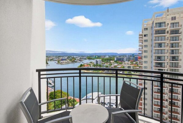 A balcony with a table and chairs, overlooking a river and cityscape. - 2BRM Panoramic Views - Chevron Renaissance (Gold Coast)