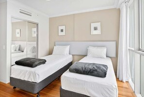 A hotel room with two single beds, a large mirror, and a window with curtains. - 2BRM Panoramic Views - Chevron Renaissance (Gold Coast)
