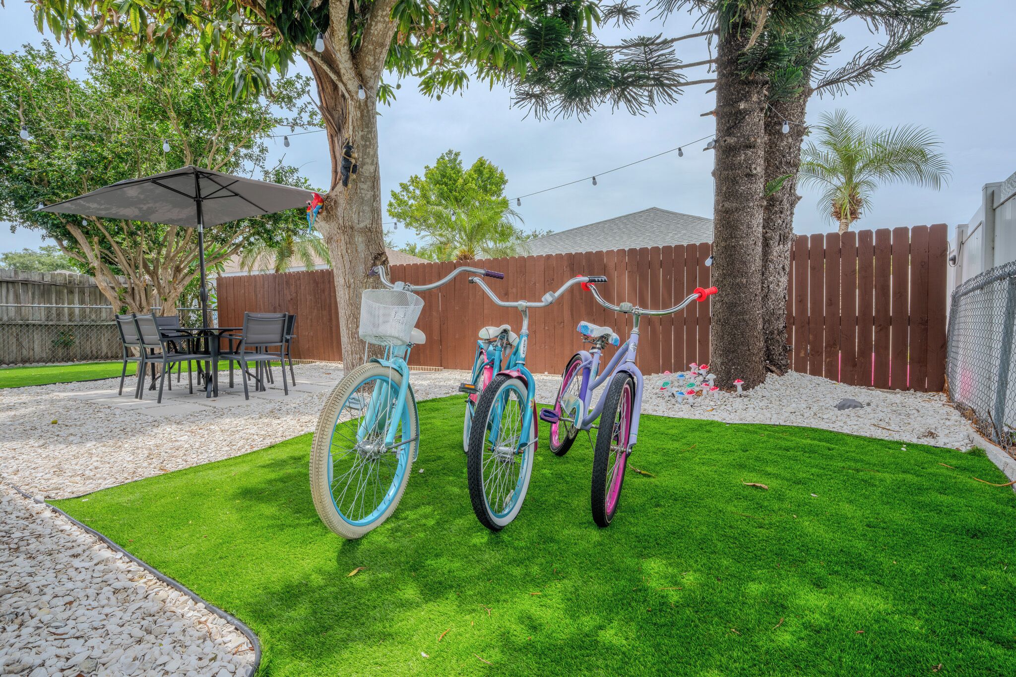 A backyard with three bicycles, a patio table with chairs, and a tree.