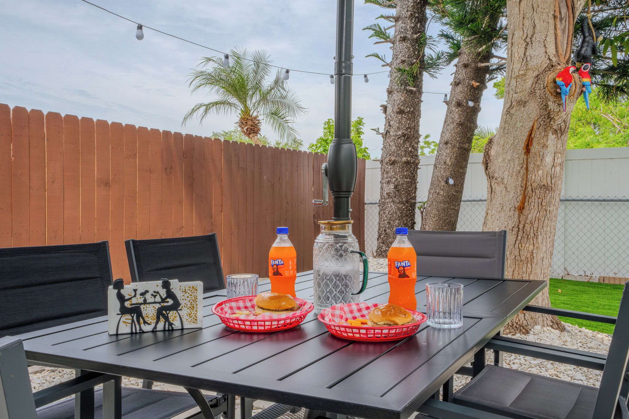 An outdoor dining table with two baskets of food, two bottles of Fanta, a glass, and a decorative item.