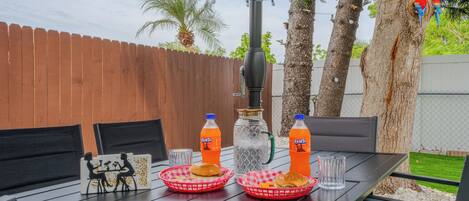 An outdoor dining table with two baskets of food, two bottles of Fanta, a glass, and a decorative item.