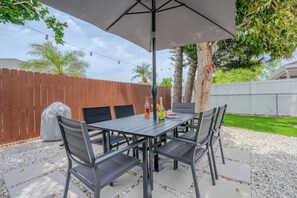 Un patio al aire libre con una mesa, sillas, una sombrilla y una parrilla.