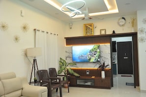 A modern living room with a flat-screen TV, a sofa, a coffee table, and a plant.