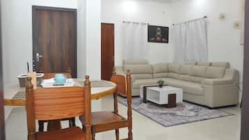 Un salon avec un canapé beige, une table à manger avec des chaises, une table basse et un tapis.