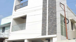 A modern two-story building with a white facade, grey stone accents, and a balcony. - Chithu Home Stay in Temple City (Kumbakonam)