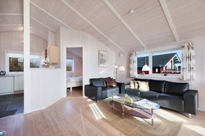 A spacious living area with a modern kitchen, a black leather sofa, and a large window with a view of a building. - Holiday home with a spa and sauna by the water (Rudkøbing)