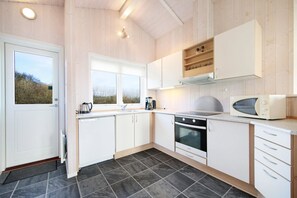 A modern kitchen with white cabinets, a built-in oven, a microwave, and a window overlooking a natural landscape. - Holiday home with a spa and sauna by the water (Rudkøbing)