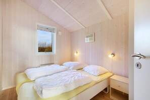 A double bed with white bedding, a bedside table, a wall-mounted light, and a window with a view of trees. - Holiday home with a spa and sauna by the water (Rudkøbing)