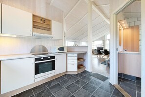 A modern kitchen with white cabinetry, a built-in oven, and a microwave. - Holiday home with a spa and sauna by the water (Rudkøbing)