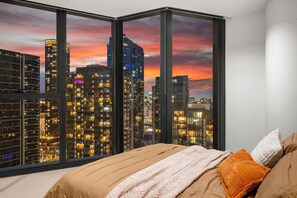 Ein Schlafzimmer mit einem großen Fenster und Blick auf die Stadt bei Einbruch der Dunkelheit.