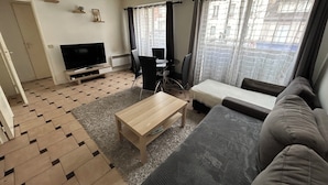 A modern living room with a sofa, a coffee table, a TV, and a dining area. - Lovely Family Stay - Two  Bedroom - Right Edge of Paris (Clichy)