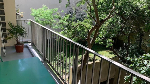 A balcony with a green table, a potted plant, and a view of a lush garden. - Lovely Family Stay - Two  Bedroom - Right Edge of Paris (Clichy)